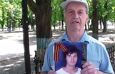 Пенсионер с фотографией погибшего внука. Кадр Anna News